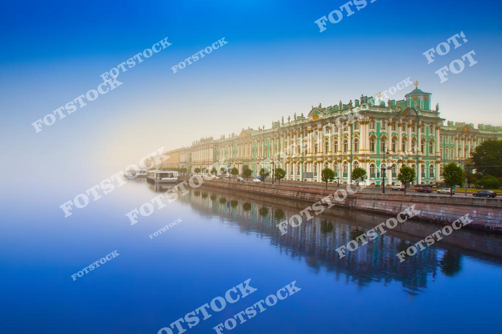 На фотографии изображён Зимний дворец, одна из главных достопримечательностей Санкт-Петербурга, расположенный на набережной реки Невы. Утренний туман создаёт мистическую атмосферу, подчёркивая красоту архитектуры XVIII века. Гладь воды отражает дворец, добавляя пейзажу изысканности. Зимний дворец является частью Эрмитажа, одного из крупнейших музеев мира.